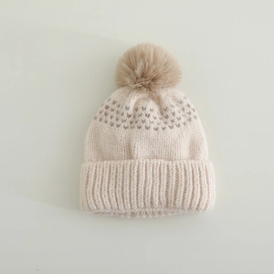 Détail du bonnet en maille crème avec texture douce et pompon en fausse fourrure brune