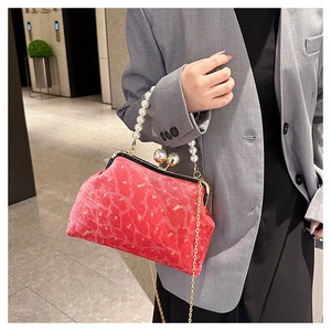 Close-up of red velvet shell bag with pearl handle and golden chain on grey blazer