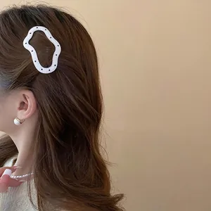 White wave hair clip with black polka dots worn on long wavy brown hair by a model