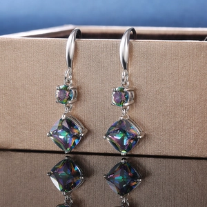 Detail of silver drop earrings with colorful zircons on a gold jewelry box edge