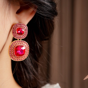 Close-up of vintage gold square earrings with red crystals on a model wearing them