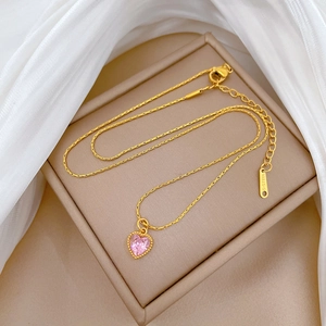 Macro view of gold heart necklace with pink gem and S-STEEL engraved tag on snake chain