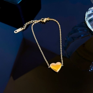 Gold stainless steel O-chain bracelet with heart pendant on dark reflective surface