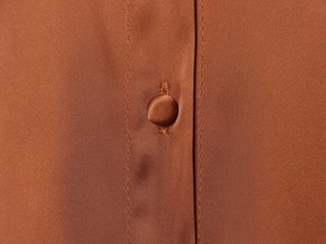 Detail shot of brown satin fabric featuring a matching fabric-covered button and texture