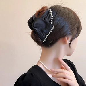 Close-up of black satin bow hair claw clip with white pearls on a model's hair