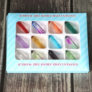 Detail of 12 mixed crystal stone pillars in a striped gift box on a wooden floor