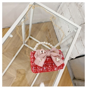 Close-up of red tweed girl's handbag with pearl handle, pink bow and gold chain strap