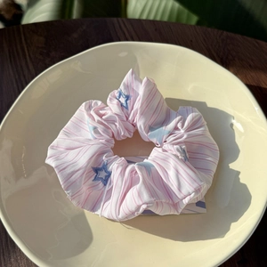 Detail of pink striped fabric scrunchie with blue star embroidery on a beige plate