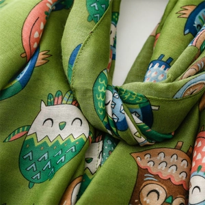 Macro view of green cotton-linen scarf showing detailed colorful owl pattern and fabric texture