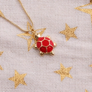 Macro view of gold-plated turtle pendant with red enamel shell on starry fabric