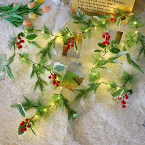 Christmas pine needle garland with red berries and warm LED lights on soft white rug