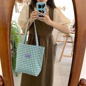 Close-up of blue and white checkered woolen tote bag with a purple logo tag on the front