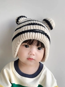 Detail of baby knit earflap hat with black and white stripes and cute pom-poms