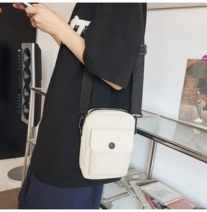 Detail view of a white canvas crossbody bag with adjustable black strap on a male model