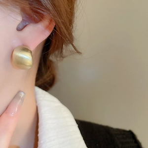 Macro close-up of golden C-shaped hoop earring with brushed metallic texture on a model