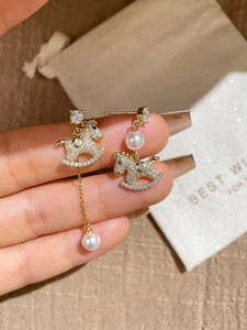 Detail of gold rocking horse earrings with pearls and pavé zircons on gift packaging