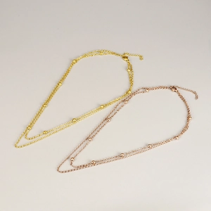 Minimalist double-layered gold and rose gold beaded titanium steel necklaces on gray background