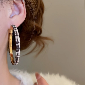 Détail de mannequin portant des créoles dorées avec un revêtement en tissu à carreaux