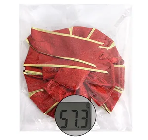 Glittery red Christmas bow with gold trim shown in protective packaging with scale weight