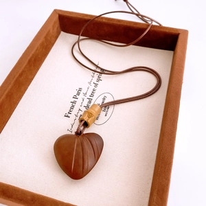 Détail du pendentif cœur en bois rétro sur cordon tressé présenté dans un plateau à bijoux