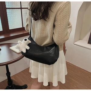 Chic black PU leather shoulder bag with cute white bear charm on a female model