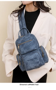 Detail of washed blue canvas chest bag with multiple bronze zipper pockets on a model