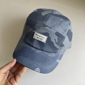 Close-up of blue camo 5-panel camper hat with white woven label and metal eyelets