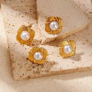 Elegant gold-plated flower wave earrings with white pearls on a textured stone surface