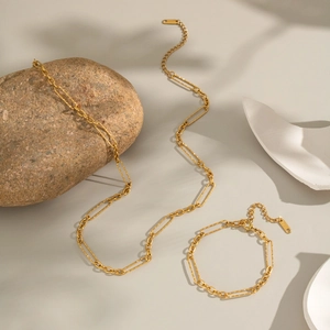 Minimalist gold plated chain necklace and bracelet set on a textured stone display