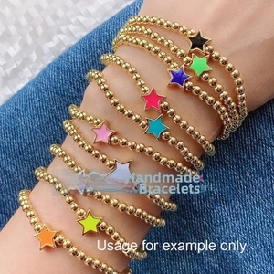 Detail of colorful enamel star charms on gold beaded bracelets worn over denim