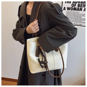 Detail of a beige tote bag with brown straps and cute charms worn with a grey coat
