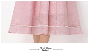 Dettaglio dell'orlo plissettato dell'abito rosa con delicate decorazioni in perle bianche
