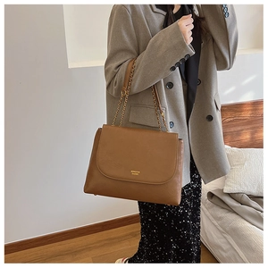 Detailed view of brown chain shoulder bag with gold lettering on elegant grey blazer