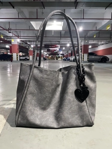 Detailed close-up of grey large tote bag with black heart pendant on concrete background