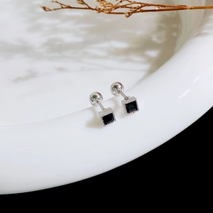 Detail of square black zircon stud earrings with screw-back on white ceramic plate