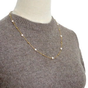 Long collier élégant en acier titane doré avec perles blanches sur un pull gris