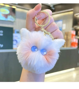 Close-up of a white plush cat keychain with blue eyes and a gold metal ring clip