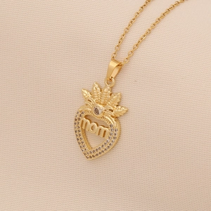 Detailed close-up of golden heart pendant with mom text and crown on beige fabric