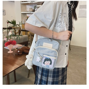 Détail d'un sac bandoulière en toile bleu clair avec pendentif ours en peluche et poches