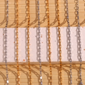 Macro shot of 18K gold and silver stainless steel box chains on a stone and wood base
