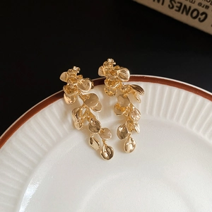 Detailed close-up of golden irregular petal fringe earrings resting on a white ceramic plate
