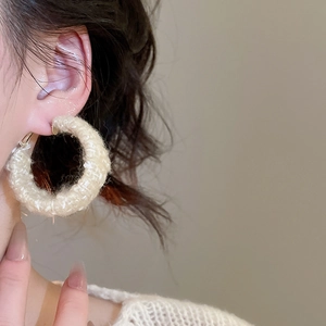 Detailaufnahme beigefarbener, gestrickter Creolen an einem Model für einen Look