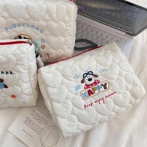 Close-up of quilted heart patterns and colorful puppy embroidery on white cosmetic bags