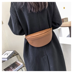 Close-up of a brown leather fanny pack styled on a model wearing a long black coat