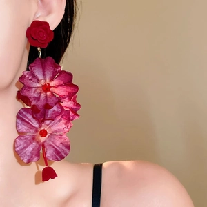 Dettaglio di orecchini a nappa con rosa in tessuto rosso e viola indossati da modella