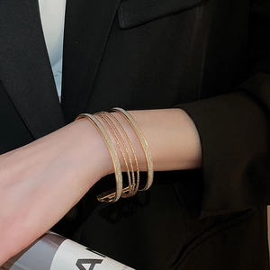 Detail of layered gold metal bracelets with sparkling textures on a chic black background