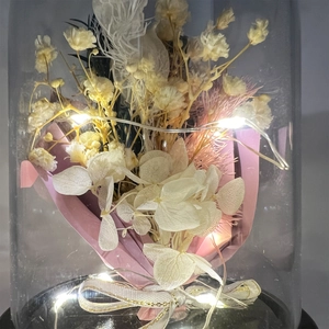 Close-up of preserved flowers in a lit plastic dome with LED lights and black base
