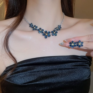 Detail shot of a model wearing a deep blue floral jewelry set with golden finish