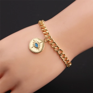 Detailed close-up of a gold-plated cuban link bracelet with a blue evil eye coin charm