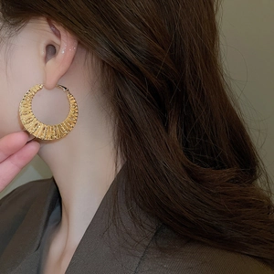 Detailed view of large gold-plated twisted hoop earring worn by a model in brown suit